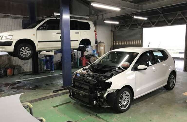 バンパーを外した車と、リフトに上げた車がある工場の作業スペース